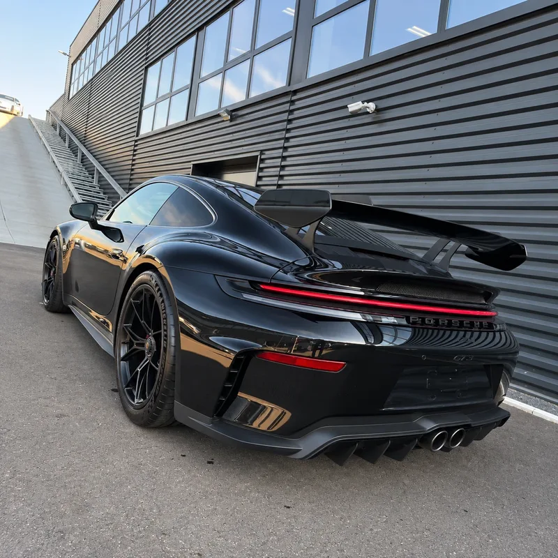 Schwarzer Porsche GT3 mit Heckflügel vor einem Industriegebäude